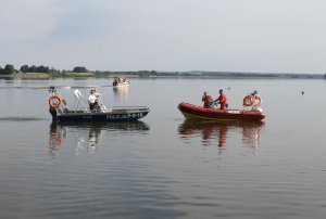 tafla wody zalewu, a na niej łódź policyjna z dwoma policjantami oraz łódź WOPR z dwoma ratownikami, w tle żaglówka