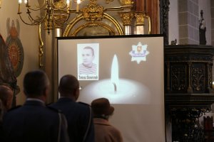 uczestnicy mszy. św., w tle widać wyświetlaną prezentację ze zdjęciem policjanta, który zginął na służbie