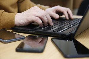 mężczyzna siedzący przy laptopie, obok smartfony na biurku